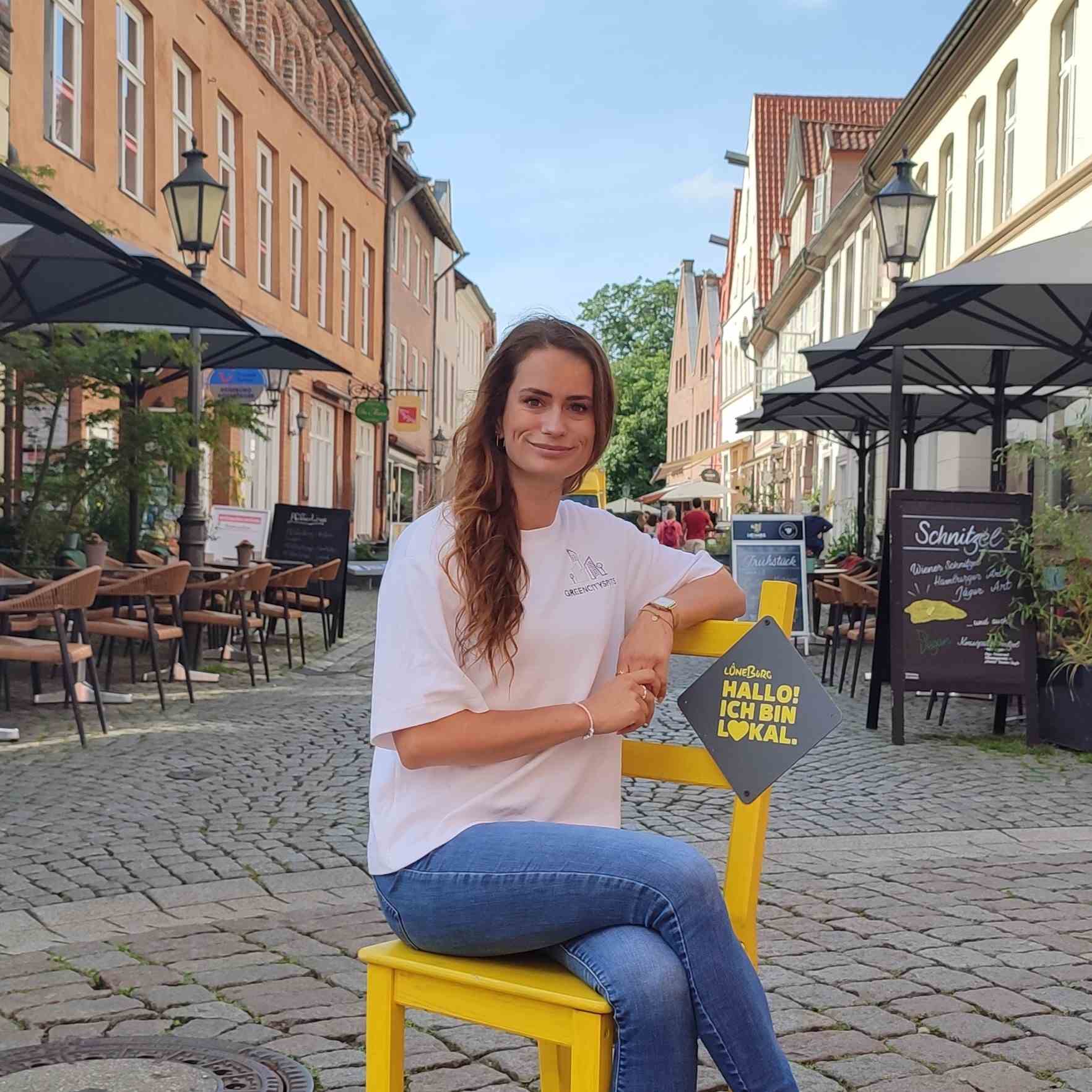 Marina von Greencityspots lächelnd lächelnd auf einem gelben Stuhl in Lüneburg